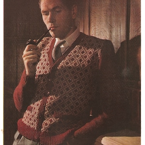 May include: A man wearing a brown and white patterned cardigan with a brown pipe in his mouth. He is wearing a white shirt with a brown and white patterned tie.