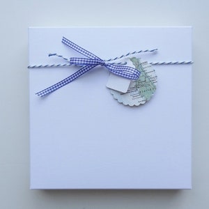 May include: A white gift box with a blue and white checked ribbon tied around it. A small map-shaped tag is attached to the ribbon.
