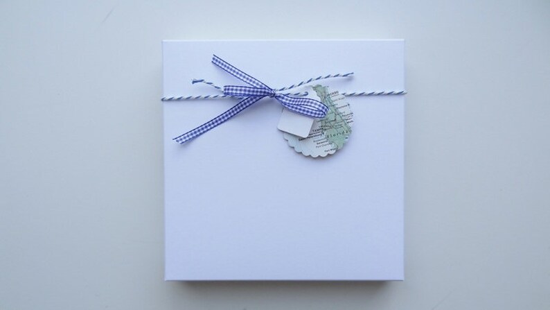 May include: A white gift box with a blue and white checked ribbon tied around it. A small map-shaped tag is attached to the ribbon.