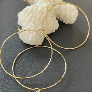 Könnte beinhalten: Drei goldfarbene Creolen. Die Ohrringe sind kreisförmig und haben ein schlichtes, elegantes Design. Die Ohrringe werden auf einem weißen, strukturierten Objekt vor dunklem Hintergrund präsentiert.