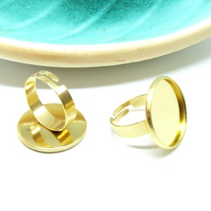 Peut inclure: Deux bagues réglables dorées avec des supports circulaires plats. Chaque bague présente un anneau en métal lisse et poli, ouvert à l'arrière pour permettre l'ajustement de la taille, et une coupelle ronde conçue pour monter des cabochons.
