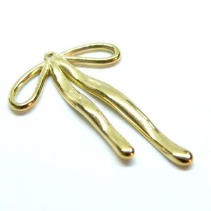 Può includere: Ciondolo a forma di fiocco in metallo dorato con finitura testurizzata. Il fiocco è composto da due anelli con un unico punto in alto.