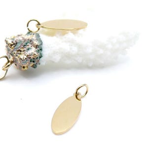 Peut inclure: Gros plan sur des breloques ovales dorées avec de petites boucles pour la fabrication de bijoux. Un charme est mis au point, tandis que d'autres sont partiellement visibles. Un morceau de corail blanc et un objet texturé doré sont en arrière-plan.