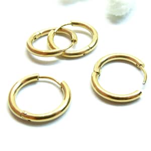 Peut inclure: Plusieurs boucles d'oreilles créoles dorées sont présentées sur un fond blanc. Les boucles d'oreilles sont circulaires, avec un fermoir à charnière. Le métal a une finition brillante. Les boucles d'oreilles varient légèrement en taille.