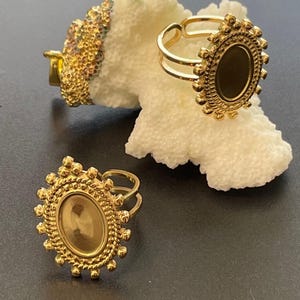 Peut inclure: Trois bagues dorées avec un centre ovale et un motif décoratif en forme d'éclat de soleil. Les bagues sont présentées sur un morceau de corail blanc sur fond sombre. Les bagues sont réglables.