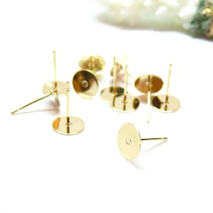 May include: A selection of gold-coloured earring posts with flat, round backings. The posts are straight and slender, designed for piercing the ear. The backings have a small hole in the centre for attaching the earring.