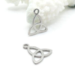 Può includere: Due ciondoli argentati a forma di nodo celtico. Ogni ciondolo presenta un design a tre punte con un anello nella parte superiore per il fissaggio ai gioielli. I ciondoli sono esposti su uno sfondo bianco con un elemento strutturato.