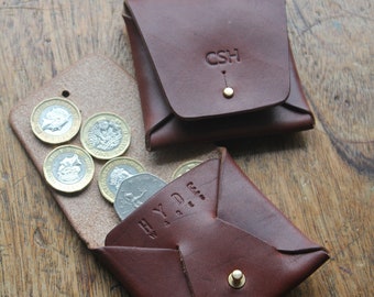 May include: Two brown leather coin purses with snap closures. The purse on the left has the initials "CSH" embossed on the front. The purse on the right has the word "HYDE" embossed on the front. Both purses are open and contain British coins.