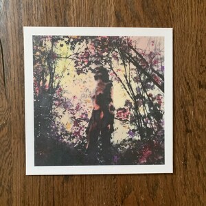 May include: A blurry image of a person standing in a forest with a colorful background of trees and flowers.