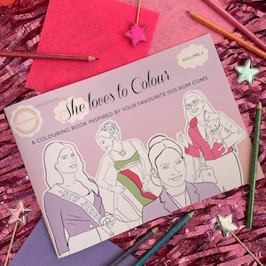Puede incluir: Una portada de libro para colorear con fondo rosa y el título "She loves to Colour" en texto blanco. El subtítulo es "A colouring book inspired by your favourite 00s rom coms". La portada presenta ilustraciones de cuatro mujeres en varias poses.