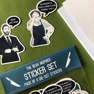 K&ouml;nnte beinhalten: Ein Set mit sechs Stanzaufklebern mit Figuren und Zitaten aus der TV-Serie "The Bear". Die Aufkleber sind in einer durchsichtigen Plastikt&uuml;te mit einer blauen Kopfzeile verpackt, auf der "The Bear Inspired Sticker Set" steht.