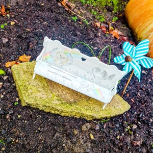 May include: White ceramic bench with a rainbow and a small angel figurine. The bench has the text "Cherished for a moment, loved for a lifetime."  A blue and white pinwheel is in the background.