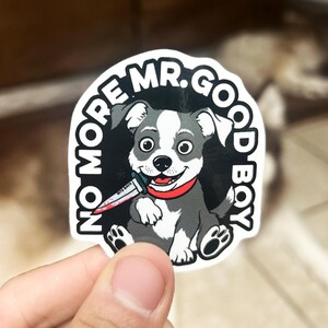 May include: A sticker featuring a cartoon dog with a knife in its mouth. The dog is gray and white with a red collar. The sticker has the text "NO MORE MR. GOOD BOY" in a circular design.