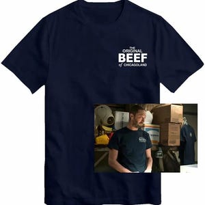 May include: A navy blue t-shirt featuring the white text "THE ORIGINAL BEEF of CHICAGOLAND". The shirt has a crew neck and short sleeves. A smaller image of a person wearing the same t-shirt is in the lower right corner.