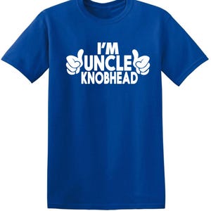 May include: Royal blue t-shirt featuring the white text "I'M UNCLE KNOBHEAD", with white cartoon thumbs-up hand gestures. The t-shirt has a crew neck design and is made of a soft material.