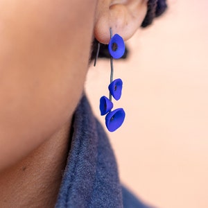 May include: A pair of dangle earrings with a blue flower design. The earrings are made of polymer clay and have a silver hook.