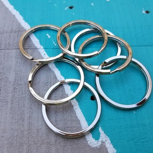 May include: A group of silver key rings, piled on top of each other, against a blue and gray background.