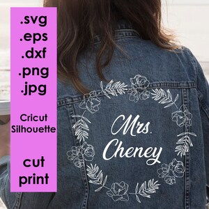 May include: A denim jacket with a white outline of a floral wreath and the text "Mrs. Cheney" on the back.