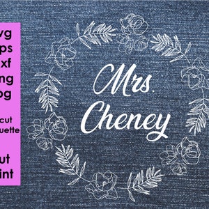 May include: White outline of a floral wreath with the text "Mrs. Cheney" in the centre on a blue denim background.