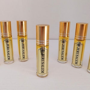 Puede incluir: Siete botellas doradas de roll-on con una etiqueta blanca que dice "JERUSALEM" con un símbolo de cruz.