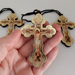 May include: Wooden Orthodox crosses with a gold border and a black cord. The crosses feature an image of Jesus Christ on the cross. The crosses have a decorative design and are made of wood.