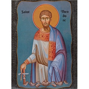 Pode incluir: Uma pintura de ícone religioso de um santo segurando uma espada. O santo é retratado com barba e veste uma túnica branca com uma capa azul. O fundo é um céu azul com uma auréola amarela ao redor da cabeça do santo. O texto "São Teodoro" está escrito nos cantos superior esquerdo e direito da pintura.