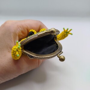 May include: A frog-shaped coin purse made of yellow and green beads. The purse has a bronze-coloured metal frame and clasp. The frog's mouth is open, showing a black interior. The frog's arms and legs are also beaded.