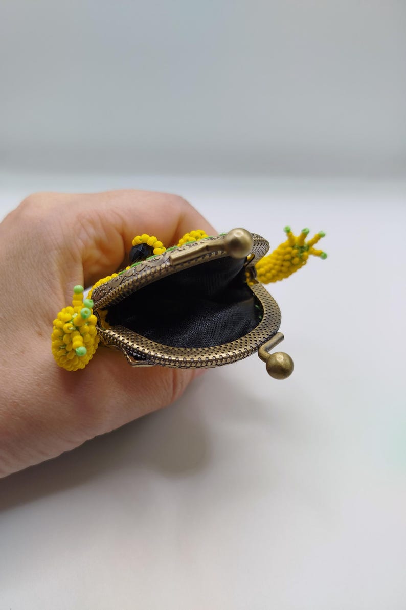 May include: A frog-shaped coin purse made of yellow and green beads. The purse has a bronze-coloured metal frame and clasp. The frog's mouth is open, showing a black interior. The frog's arms and legs are also beaded.