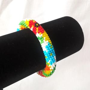 May include: A colorful beaded bracelet with a floral pattern. The bracelet is made of small, round beads in shades of red, yellow, green, blue, and white. The beads are arranged in a repeating pattern of flowers.