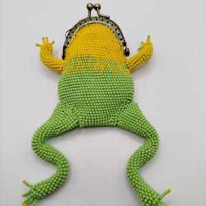 May include: A beaded frog-shaped coin purse with a metal clasp. The purse has a yellow head and arms, a green body and legs, and yellow accents on the feet. The design is intended to resemble a frog.