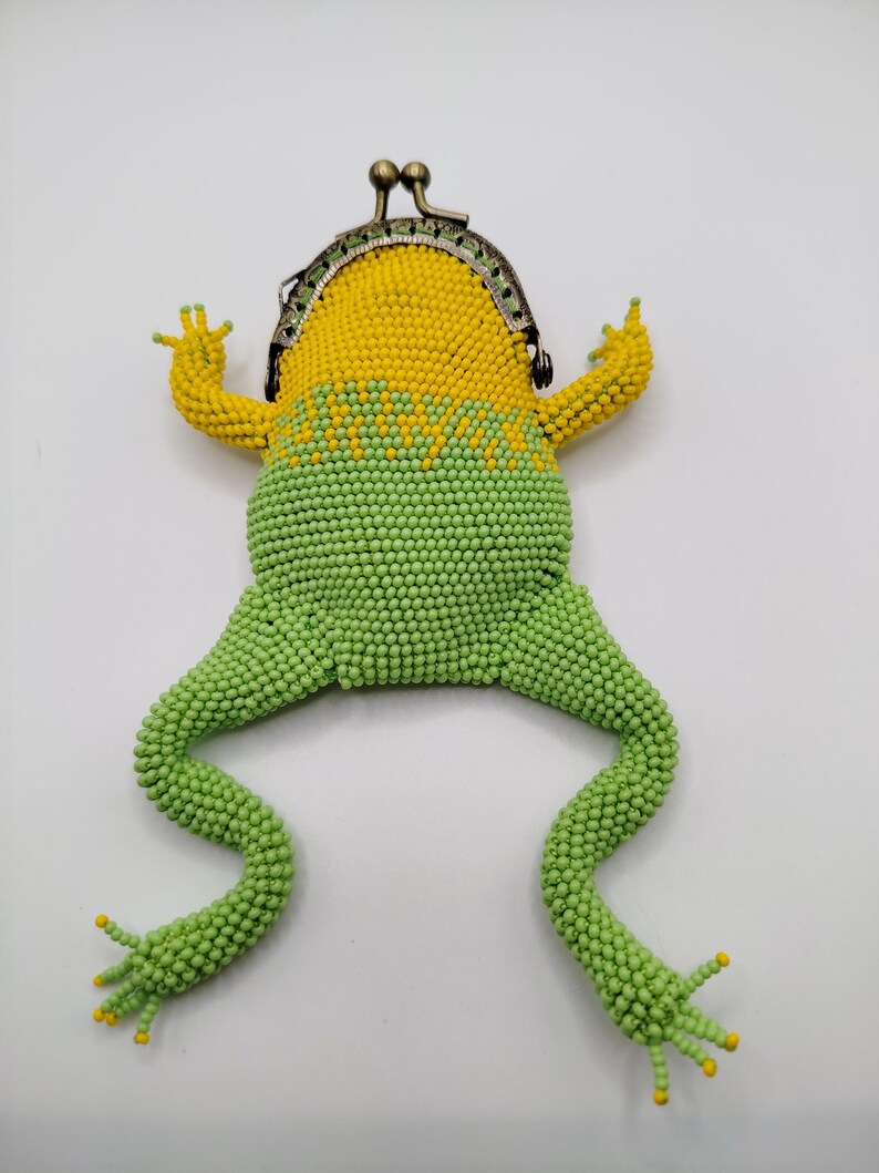 May include: A beaded frog-shaped coin purse with a metal clasp. The purse has a yellow head and arms, a green body and legs, and yellow accents on the feet. The design is intended to resemble a frog.