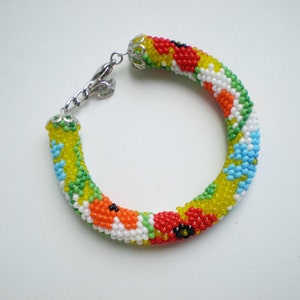 May include: A colorful beaded bracelet with a floral pattern in shades of red, yellow, green, blue, and white. The bracelet has a silver clasp.