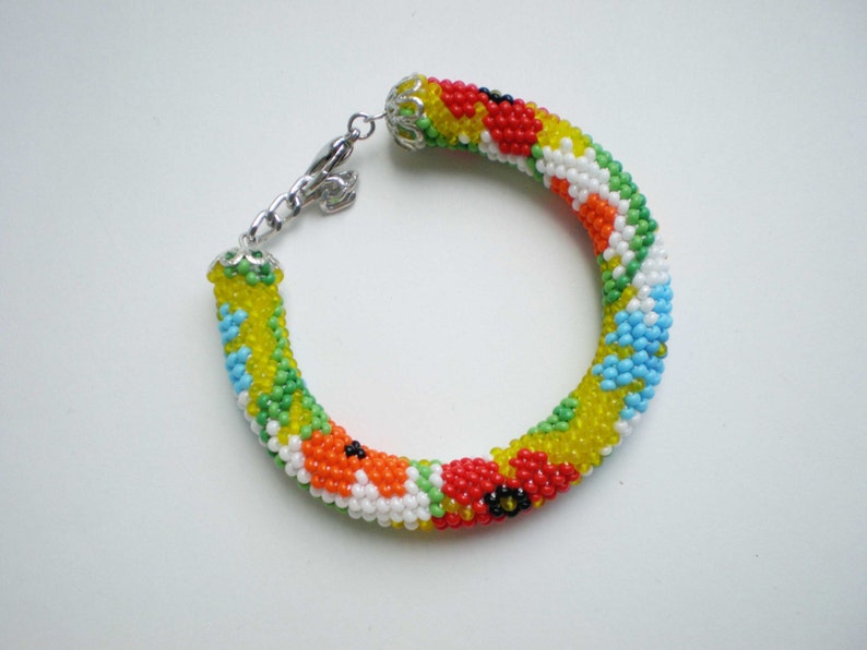 May include: A colorful beaded bracelet with a floral pattern in shades of red, yellow, green, blue, and white. The bracelet has a silver clasp.