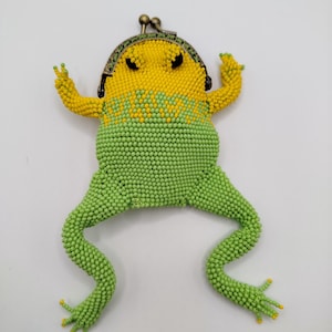 May include: A novelty coin purse in the shape of a frog, made from beads. The purse is predominantly green and yellow, with a metal clasp at the top. The frog design includes beaded legs and arms, creating a fun and quirky accessory.
