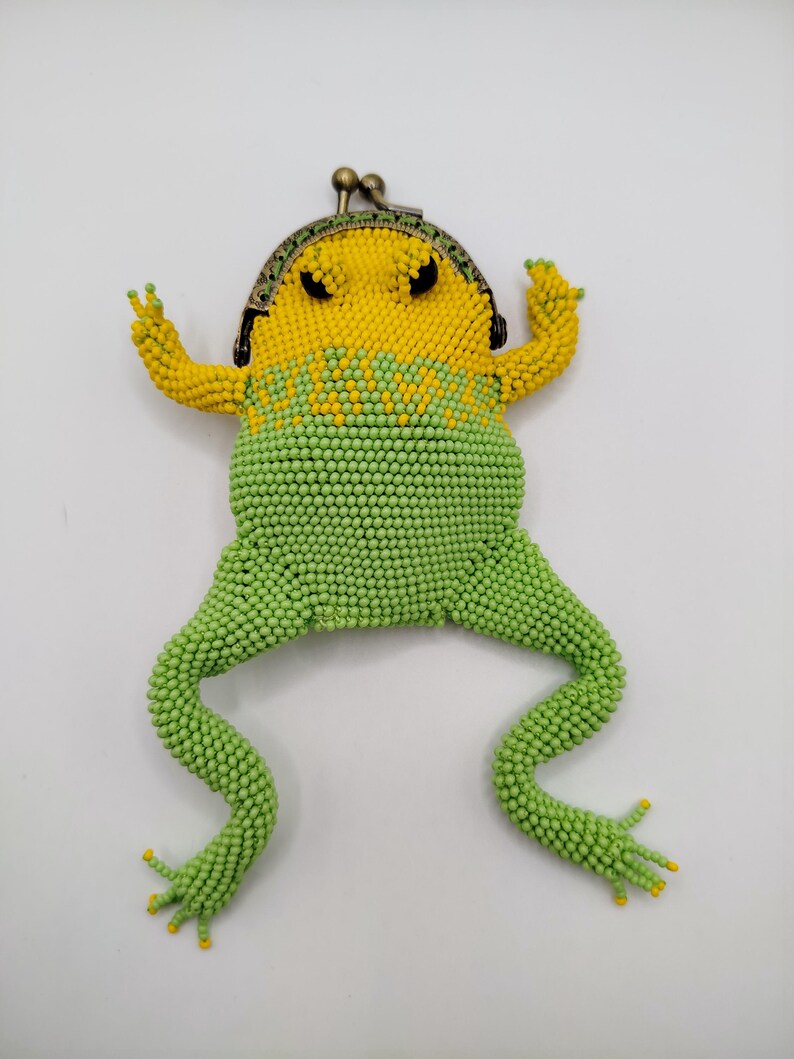 May include: A novelty coin purse in the shape of a frog, made from beads. The purse is predominantly green and yellow, with a metal clasp at the top. The frog design includes beaded legs and arms, creating a fun and quirky accessory.
