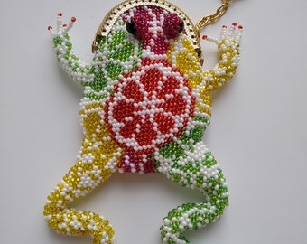May include: A beaded frog keychain with a gold coin purse. The frog is made of white, yellow, green, red, and pink beads. The frog has a red and black eye.