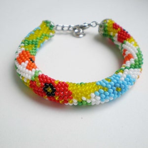 May include: A colorful beaded bracelet with a floral pattern. The bracelet is made with small, round beads in shades of red, yellow, blue, green, and white.