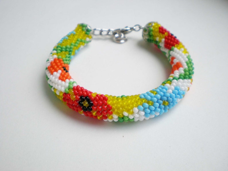 May include: A colorful beaded bracelet with a floral pattern. The bracelet is made with small, round beads in shades of red, yellow, blue, green, and white.