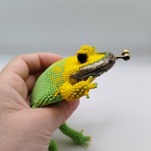 May include: A beaded frog-shaped coin purse in yellow and green. The frog's body is crafted with small beads, featuring a yellow head and a green body. The purse has a metal clasp and green beaded legs.