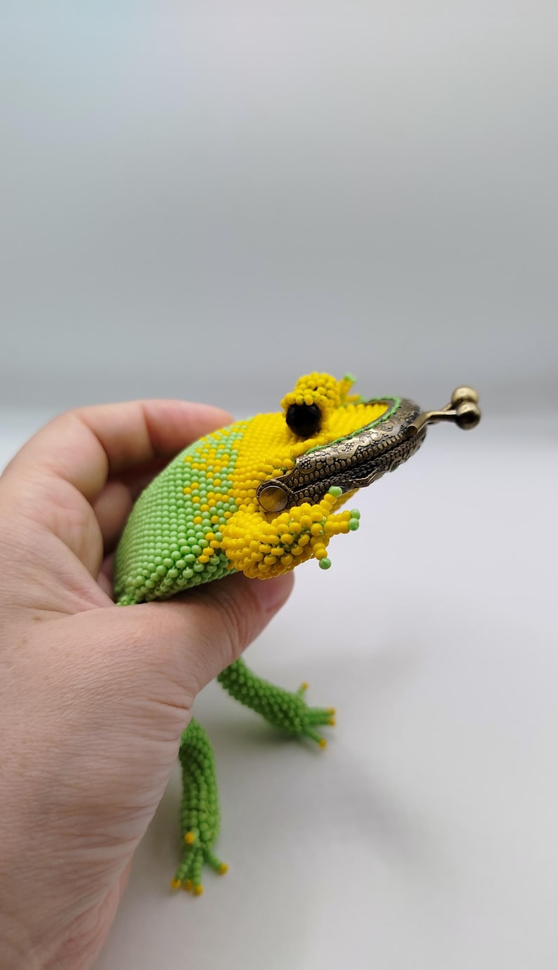 May include: A beaded frog-shaped coin purse in yellow and green. The frog's body is crafted with small beads, featuring a yellow head and a green body. The purse has a metal clasp and green beaded legs.