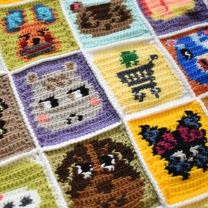 May include: A crocheted blanket with a variety of colorful squares featuring animal characters. Each square is outlined in white and features a different animal, including a bunny, a bear, a deer, a cat, and a dog.