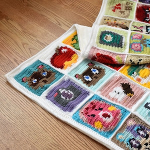 May include: A white crocheted blanket with colorful squares featuring various animal and object designs. The squares are stitched together to create a larger blanket.