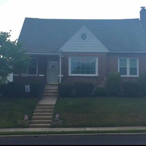 Puede incluir: Una casa de ladrillo con un techo gris y una puerta delantera blanca. La casa tiene dos ventanas en la parte delantera y una peque&ntilde;a ventana en el hastial. Hay un c&eacute;sped verde delante de la casa con un conjunto de escaleras que conducen a la puerta delantera.