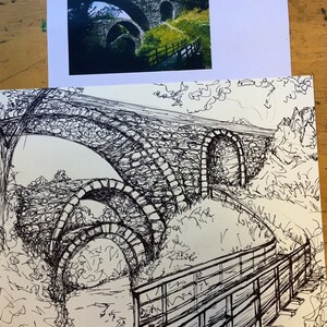 Puede incluir: Un dibujo en tinta negra y blanca de un puente de piedra con m&uacute;ltiples arcos. El puente est&aacute; rodeado de &aacute;rboles y arbustos. Una pasarela de madera con barandilla conduce al puente.