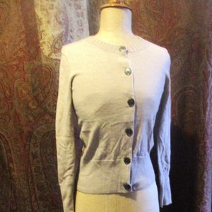 May include: A light gray cardigan with a button-up front. The cardigan is on a mannequin and has a ribbed texture.