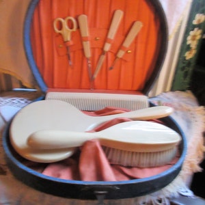 May include: A vintage blue vanity case with a red interior. The case contains a comb, a brush, and a set of manicure tools.