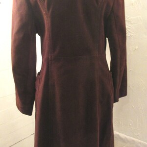 May include: A long, burgundy suede coat with a white fur collar and trim. The coat has a long, flowing silhouette and a classic design.