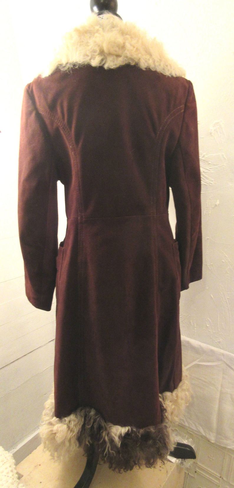 May include: A long, burgundy suede coat with a white fur collar and trim. The coat has a long, flowing silhouette and a classic design.