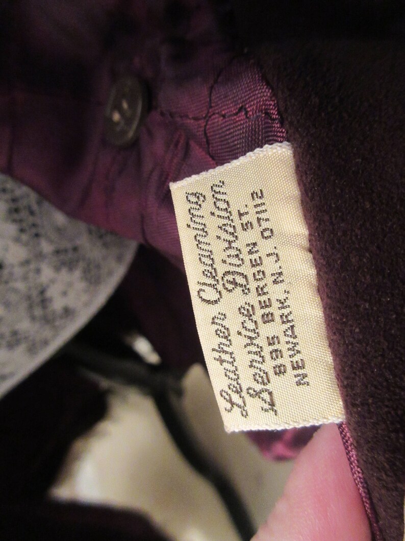 May include: A close-up of a brown leather label with white text that reads "Leather Cleaning & Service Division 835 Bergen St. Newark, N.J. 07112"