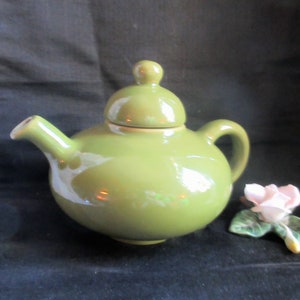 Könnte beinhalten: Eine grüne Teekanne aus Keramik mit rundem Korpus und Deckel. Die Teekanne hat einen Ausguss und einen Henkel.